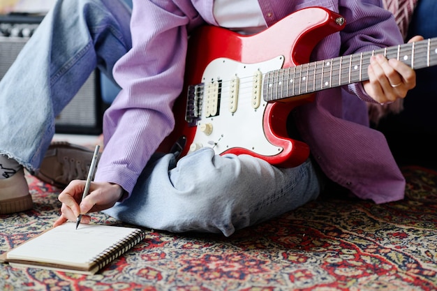 Primer plano de un músico sentado en el suelo con guitarra y escribiendo una nueva canción