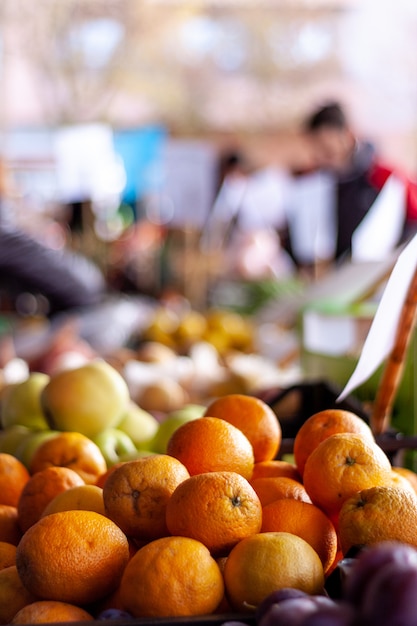 Foto primer plano de naranjas y otras frutas en un puesto en el mercado con algunas personas