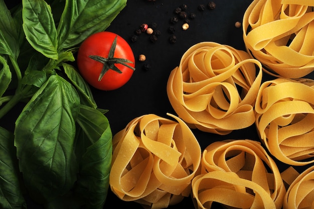 Primer plano de nidos de pasta en superficie negra con tomate y albahaca