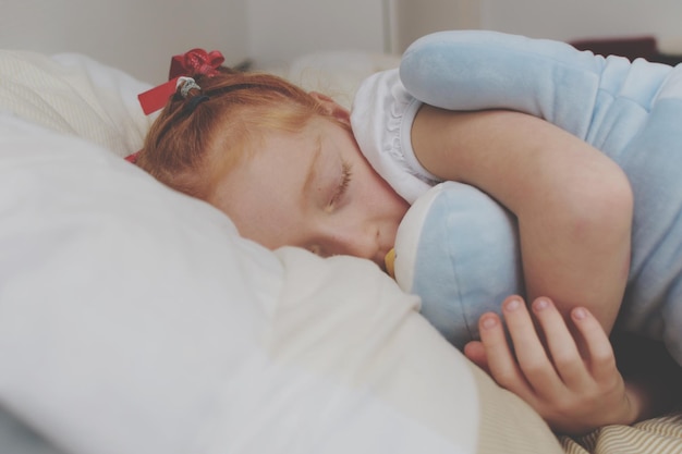 Primer plano de una niña abrazando un juguete de peluche mientras duerme en la cama en casa