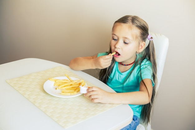 Primer plano de una niña comiendo papas fritas en la cocina