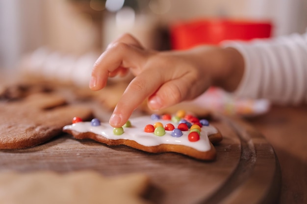 Primer plano de una niña con gorro de Papá Noel decora el pan de jengibre con perlas multicolores nuevas y navideñas