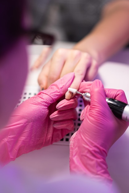 Foto primer plano de una niña haciendo una manicura en un salón de belleza cuidado de uñas manicurista en guantes rosas quita el esmalte de gel de las uñas con un fresco procedimiento cosmético de primer plano de manicura de hardware