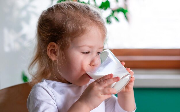 El primer plano de una niña linda bebiendo leche, desayunando con un vaso de leche caliente por la mañana