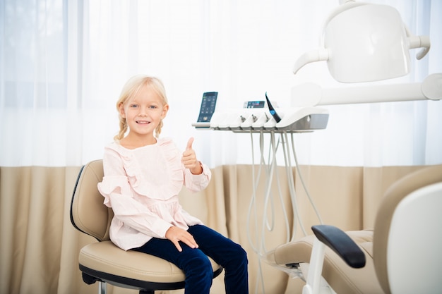 Un primer plano de una niña en una oficina de dentista mostrando los pulgares para arriba.