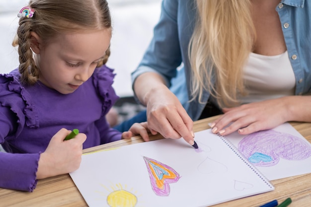 Primer plano de la niña pintando en casa con mamá usando crayones y lápices Regreso a la escuela