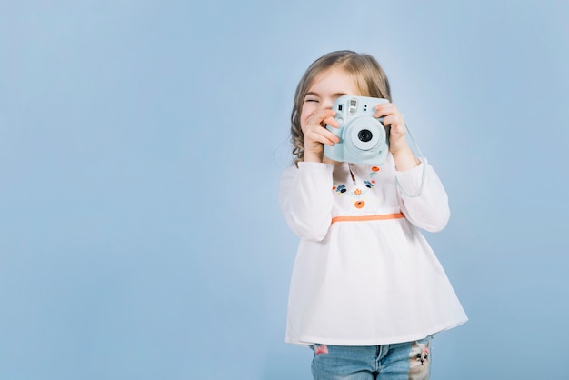 Primer plano de una niña que captura la foto con una cámara instantánea contra el fondo azul