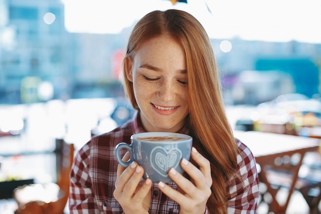 Primer plano de niña rojiza natural disfrutando de una gran taza de café