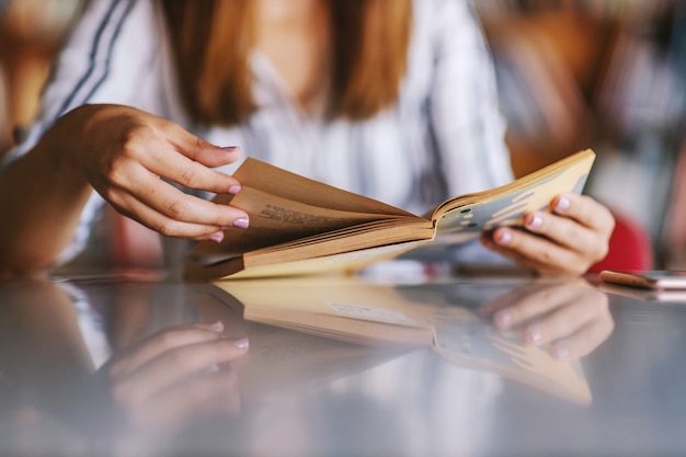 Primer plano de una niña sentada en la biblioteca y leyendo un libro.