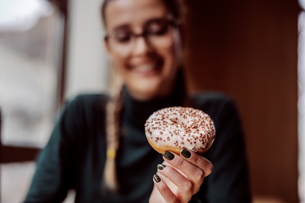 Primer plano de una niña sosteniendo donut mientras está sentado en la pastelería.