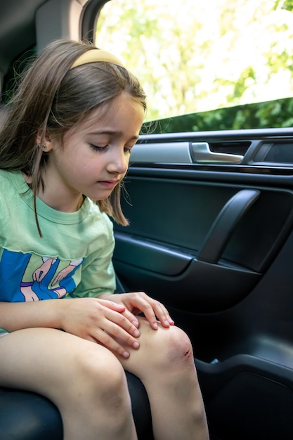 El primer plano de una niña sosteniendo su rodilla herida magullada con las manos