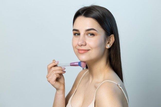 Primer plano de una niña en un top ligero sobre un fondo blanco haciendo un maquillaje facial