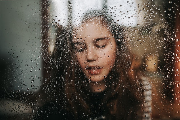 Primer plano de una niña vista a través de una ventana húmeda en la temporada de lluvias