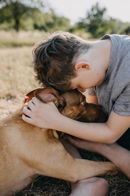 Primer plano de un niño abrazando a un perro pit bull cerca tocando frentes