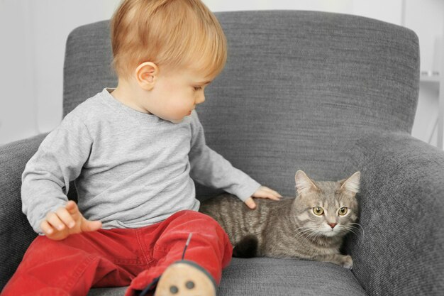 El primer plano de un niño adorable con un lindo gato en un sillón gris