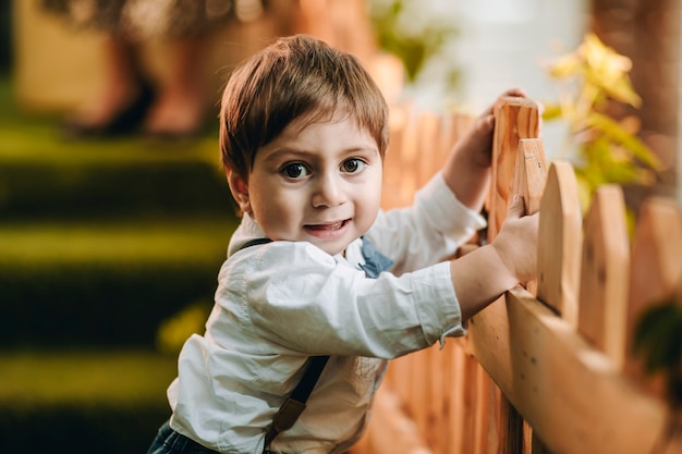 Primer plano de un niño alegre en el patio de recreo sosteniendo desde la valla de madera