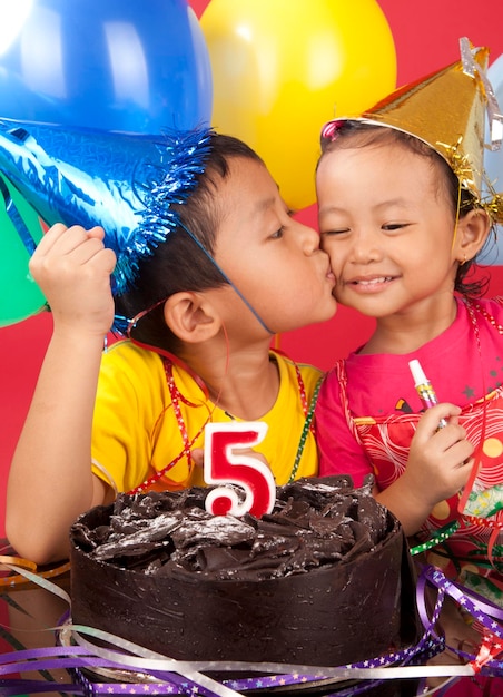 Foto primer plano de un niño besando a su hermana mientras está de pie junto al pastel de cumpleaños en una fiesta