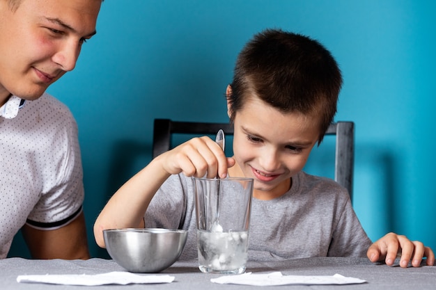 Primer plano de un niño con una camiseta gris lava un pincel de pintura de acuarela sobre un fondo azul.