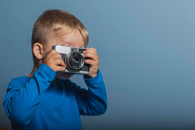 Foto primer plano de un niño fotografiando con una cámara contra un fondo azul