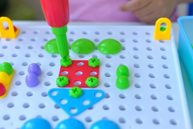 Foto primer plano de un niño jugando un rompecabezas de constructor educativo para niños con un destornillador, un destornillador y shurukas con fiugs geométricos multicolores. concepto de desarrollo creativo para niños en edad preescolar.