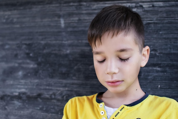 Foto primer plano de un niño con los ojos cerrados por una pared de madera negra