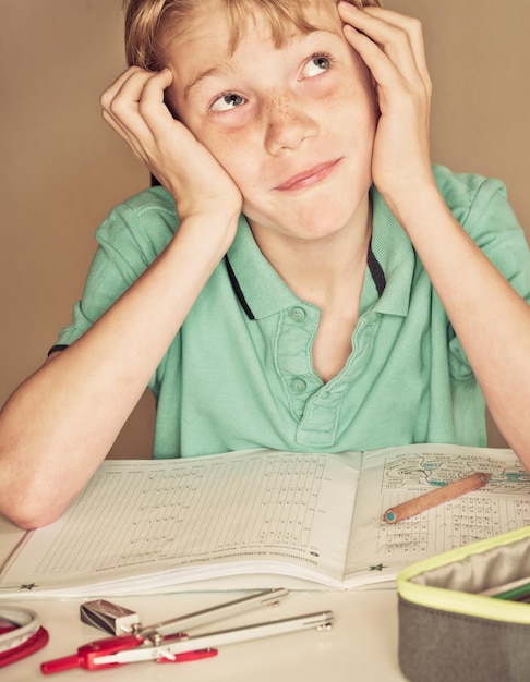 Primer plano de un niño pensativo estudiando en la mesa contra la pared