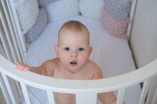 Primer plano de un niño pequeño de pie en una cuna, el niño no quiere dormir en la cama