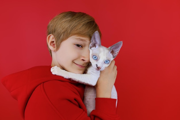 El primer plano de un niño que sostiene un pequeño gato blanco se inclinó contra él y abraza suavemente al gato