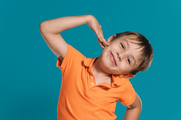 Primer plano de un niño rubio en una camiseta naranja posando con una sonrisa en su rostro sobre un fondo azul.