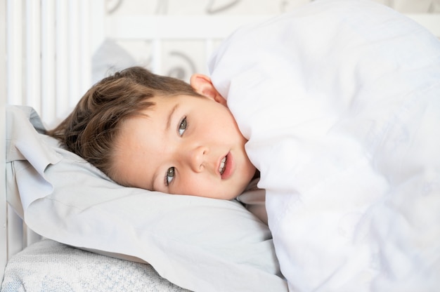 Primer plano de un niño soñoliento en la cama, niño solitario.