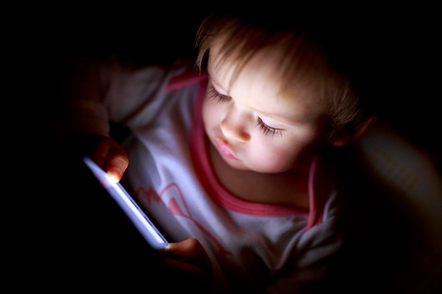 Primer plano de un niño usando una tableta digital en un cuarto oscuro