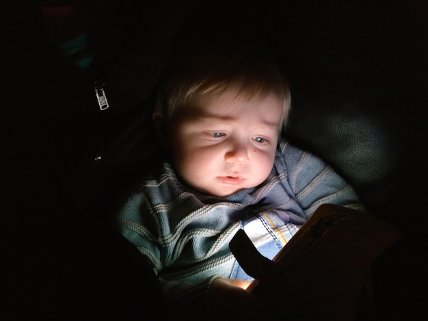 Primer plano de un niño usando un teléfono móvil en el cuarto oscuro