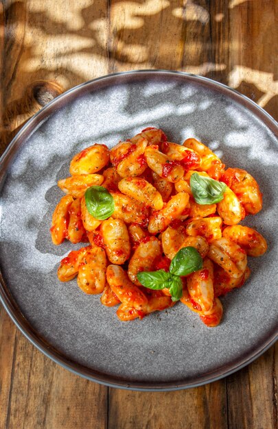 Primer plano de ñoquis de patata italianos con salsa de tomate y albahaca fresca en placa gris sobre fondo de madera