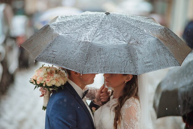 Primer plano de la novia y el novio caminando bajo el paraguas en el día de su boda