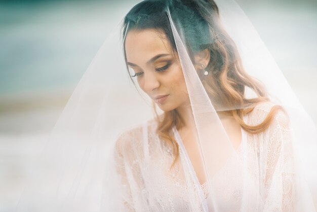 Primer plano de la novia bajo un velo sobre un fondo de cielo azul y mar negro