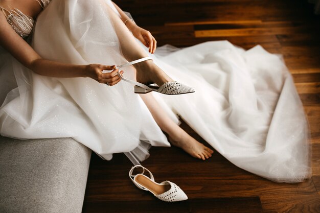 Primer plano de una novia en vestido blanco, poniéndose zapatos planos de boda
