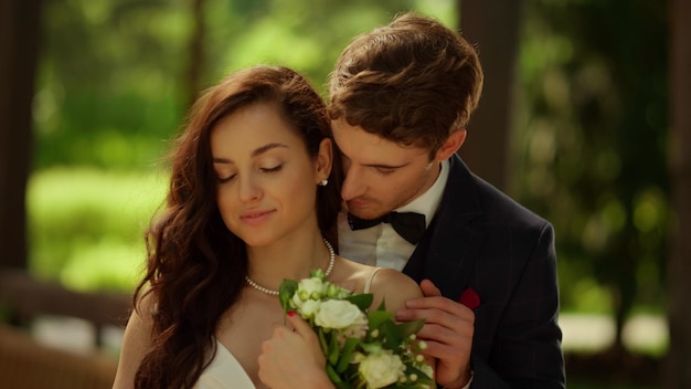 Primer plano novio caliente de pie detrás de la novia en la ceremonia de la boda en el parque Retrato de hombre sexy besando el hombro de la mujer al aire libre Pareja amorosa posando en el jardín