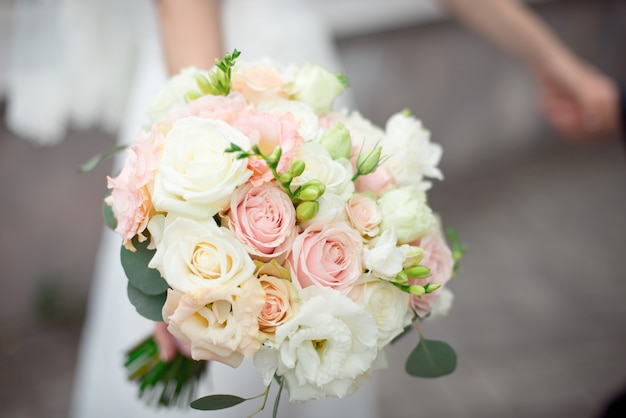 Primer plano novio en un traje y la novia en un vestido blanco están de pie y sosteniendo un ramo de rosas de durazno, eustomas y flores y vegetación