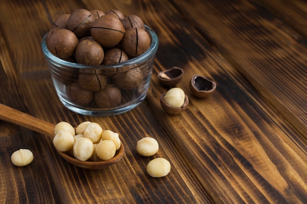 Primer plano de nueces de macadamia en una cuchara de madera y un arco de vidrio sobre la mesa