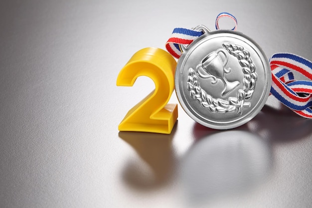 Primer plano del número 2 con medalla de plata sobre un fondo gris