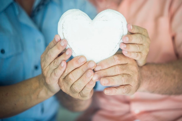 Foto primer plano del objeto de decoración de madera en forma de corazón concepto de estilo de vida saludable para personas mayores concepto de ataque al corazón amor y relación con las manos de un hombre y una mujer viejos y maduros juntos para siempre vida citas