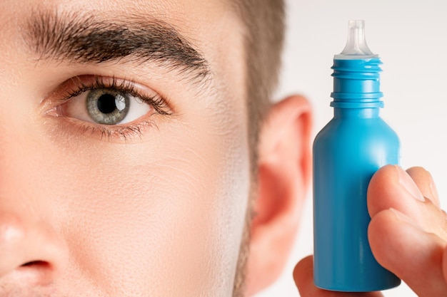 Primer plano del ojo masculino y una pequeña botella de gotas para los ojos