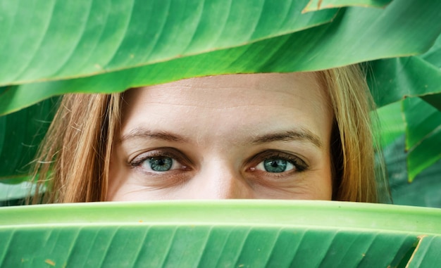 El primer plano de los ojos de una mujer joven mirando desde las hojas de las palmeras