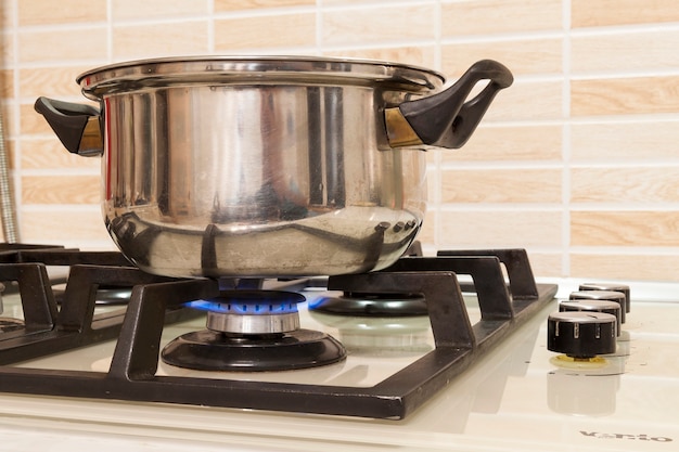 Primer plano de la olla de acero inoxidable en la estufa de gas en la cocina casera moderna y contemporánea. Enfoque selectivo en la olla.