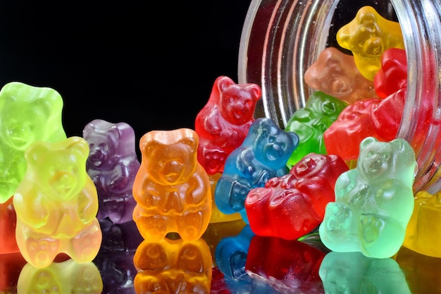 Primer plano de osos de goma multicolores derramándose de un frasco de vidrio sobre un fondo negro