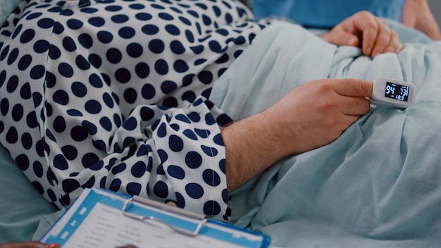 Primer plano de un paciente enfermo descansando en la cama con oxímetro médico en el dedo