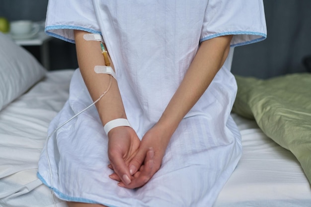 Primer plano de una paciente joven con catéter en el brazo sentada en la cama en la sala