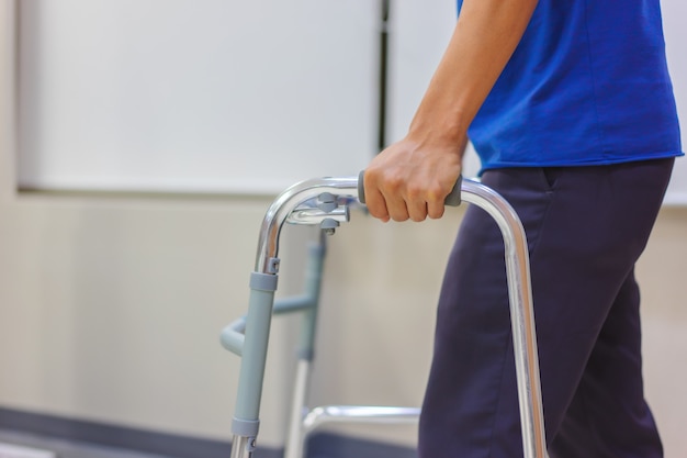 Primer plano, paciente masculino de mediana edad está utilizando caminantes para practicar caminar después de la cirugía.