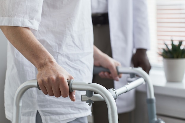 Primer plano del paciente mayor caminando con andador a lo largo de la sala del hospital