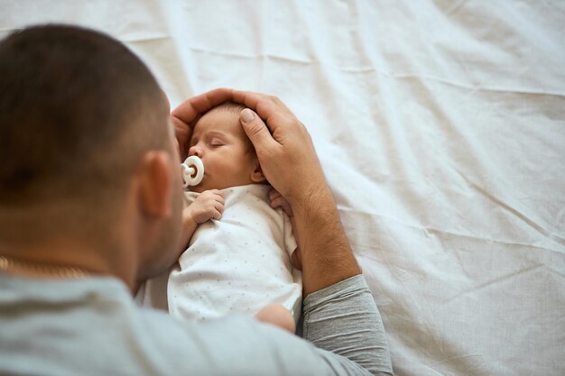 Primer plano de un padre irreconocible sosteniendo la cabeza del bebé dormido